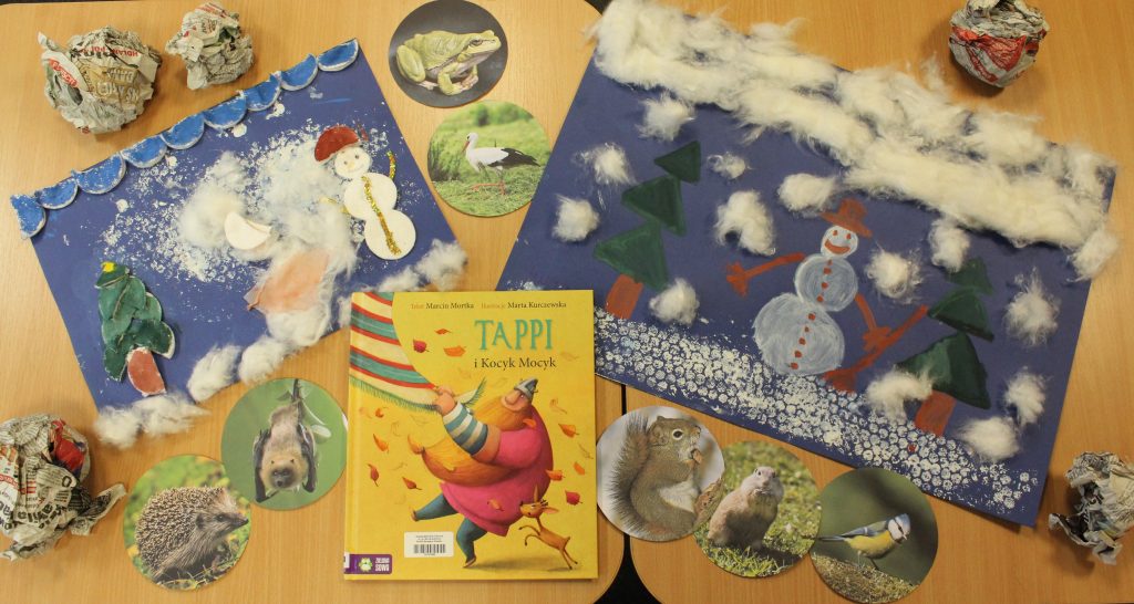 Na zdjęciu 2 prace plastyczne z zimowym krajobrazem wykonane z użyciem farb, waty, folii i tkaniny, książkę Marcina Mortki "Tappi i Kocyk Mocyk", zdjęcia zwierząt oraz kule z gazet. 